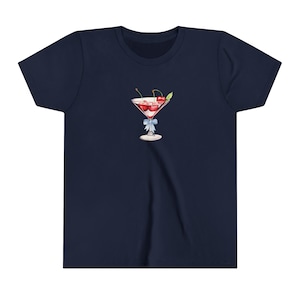Peut inclure: T-shirt bleu marine avec une illustration &agrave; l'aquarelle d'un verre &agrave; cocktail rempli de cerises. Le verre est orn&eacute; d'un ruban bleu clair nou&eacute; autour de la tige. Les cerises sont rouges et la boisson est rose.