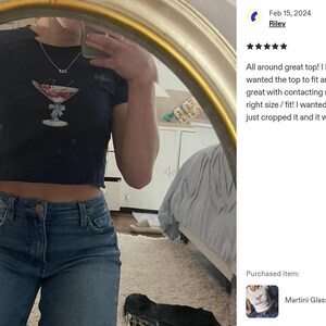 Peut inclure: Haut court bleu marine avec un motif de verre &agrave; martini et une cerise. Le haut est port&eacute; avec un jean bleu. L'image est refl&eacute;t&eacute;e dans un miroir.