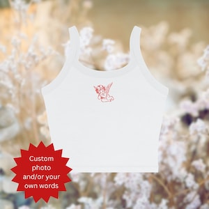 Puede incluir: Top blanco de tirantes con un gr&aacute;fico de &aacute;ngel rojo. El top es de estilo corto y tiene un escote redondo. El texto "Custom photo and/or your own words" est&aacute; en una estrella roja.