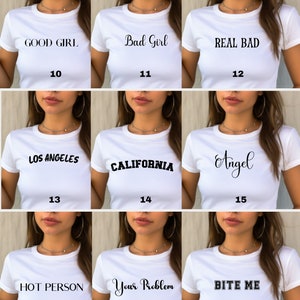 Puede incluir: Nueve camisetas blancas con diferentes dise&ntilde;os de texto negro. Los dise&ntilde;os incluyen "GOOD GIRL", "Bad Girl", "REAL BAD", "LOS ANGELES", "CALIFORNIA", "Angel", "HOT PERSON", "Your Problem" y "BITE ME".