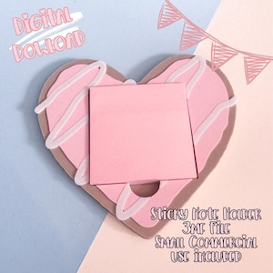 Op de afbeelding: Een hartvormige sticky note houder in een donut ontwerp met roze glazuur en witte glazuur drizzle. De houder heeft een vierkant roze notitieblok in het midden. Tekst op de afbeelding luidt "Digital Download" en "Sticky Note Holder 3MF File Small Commercial Use Included."