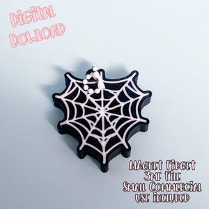 Pode incluir: Um fidget magnético em forma de teia de aranha preta e branca com uma pequena corrente. As palavras "Digital Download" estão em script rosa no canto superior esquerdo. As palavras "Magnet Fidget 3MF File Small Commercial Use Included" estão em script rosa no canto inferior direito.