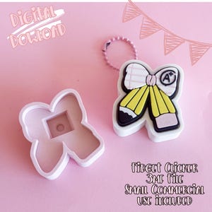 Op de afbeelding: Een wit en gele potlood-thema fidget clicker met een roze sleutelhanger en een bijpassende mal. De clicker heeft een strik ontwerp met een "A+" symbool. De tekst "Digital Download" en "Fidget Clicker 3MF File Small Commercial Use Included" zijn ook zichtbaar.