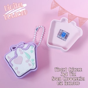 May include: A pink background features a digital download graphic. A light purple playing card-shaped keychain with a bow and heart design is attached to a white beaded chain. A light pink container holds a blue switch. Text reads "Fidget Clicker 3MF File Small Commercial Use Included."