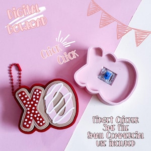 May include: A pink fidget clicker with a blue switch and a red XO keychain. The XO keychain is red with white polka dots and a donut-shaped O with pink icing. Text includes "Digital Download" and "Click Click".