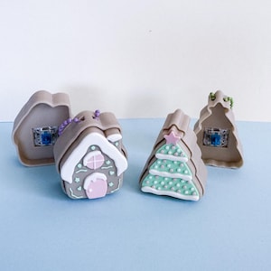 May include: Four miniature Christmas decorations. Two are shaped like gingerbread houses, one with a pink door and the other with a Christmas tree design. The other two are gingerbread house shapes with a blue light inside. All are tan, white, pink, and green.
