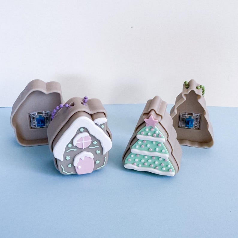 May include: Four miniature Christmas decorations. Two are shaped like gingerbread houses, one with a pink door and the other with a Christmas tree design. The other two are gingerbread house shapes with a blue light inside. All are tan, white, pink, and green.
