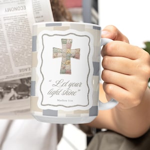Può includere: Tazza in ceramica bianca con un design a croce patchwork e il testo "Let your light shine" da Matteo 5:16. La tazza ha un motivo a quadri grigio chiaro e beige e un manico bianco.