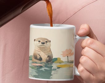 Può includere: Tazza in ceramica bianca con una lontra in uno stagno con ninfee e un fiore rosa. La lontra è marrone chiaro con la pancia bianca. Il caffè viene versato nella tazza.