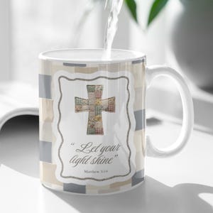 May include: White ceramic mug with a patchwork cross design. The mug features the quote "Let your light shine" from Matthew 5:16. The background has a patchwork pattern in neutral tones.