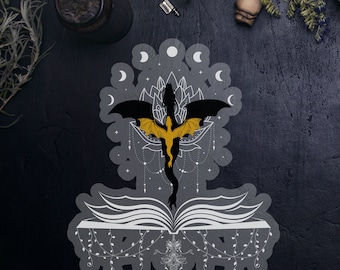May include: A black and gold dragon silhouette with wings spread, rising from an open book. The dragon is surrounded by a circle of moons and a floral design. The book is decorated with a dangling chain of leaves and a sword.