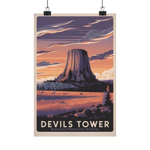 Könnte beinhalten: Ein Poster mit einer stilisierten Illustration des Devils Tower in Wyoming. Das Kunstwerk zeigt den Turm unter einem Sonnenuntergangshimmel mit Orange-, Lila- und Blautönen. Der Text "Devils Tower" und "Bear Lodge Mountains, Wyoming" befindet sich unten.