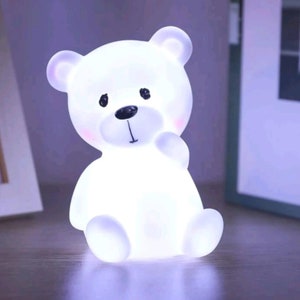 May include: White teddy bear night light with a black nose and eyes. The light is on and illuminating the bear.