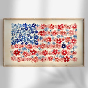 Puede incluir: Pintura a la acuarela de la bandera estadounidense, compuesta por flores rojas, blancas y azules. La obra de arte está enmarcada en un marco de madera clara, creando una exhibición patriótica y artística. Las flores están dispuestas para imitar el diseño de la bandera.