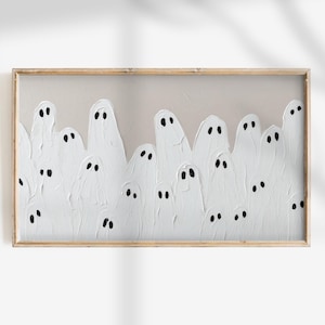 May include: A framed artwork featuring a textured, off-white background with a gathering of white ghost figures. Each ghost has two black dot eyes. The artwork is encased in a light brown wooden frame, creating a Halloween theme.