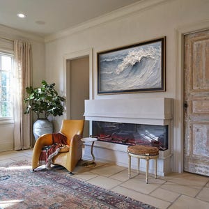 Op de afbeelding: Een woonkamer met een moderne open haard, een gele leren fauteuil en een groot ingelijst schilderij van een golf. De kamer heeft een vloerkleed, een bijzettafel, een decoratieve kruk en een grote plant in een keramische vaas. De deur is verweerd.