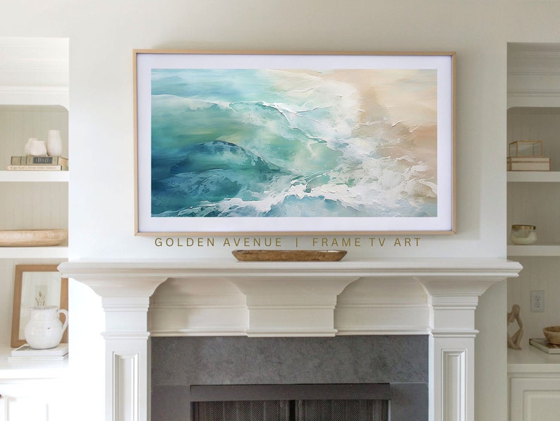 May include: Abstract painting of ocean waves in shades of blue, green, and white, framed in a light wood frame, hanging above a white fireplace mantel. The text "GOLDEN AVENUE | FRAME TV ART" is below the painting.