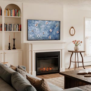 Op de afbeelding: Een woonkamer met een open haard, een grote tv met een zwembadsc&egrave;ne en ingebouwde boekenkasten. Een bank met kussens met patronen en een houten salontafel met een boek en een vaas met bloemen maken het gezellige interieur compleet.
