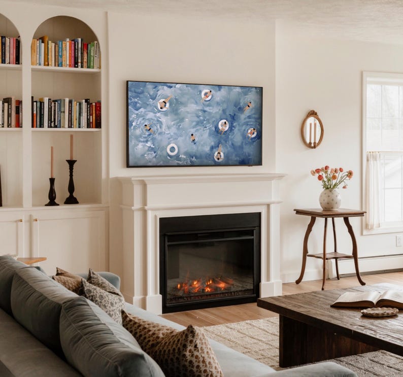 Op de afbeelding: Een woonkamer met een open haard, een grote tv met een zwembadsc&egrave;ne en ingebouwde boekenkasten. Een bank met kussens met patronen en een houten salontafel met een boek en een vaas met bloemen maken het gezellige interieur compleet.