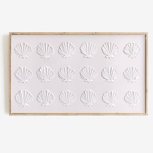 May include: A framed wall art piece with a white background and 18 raised white seashells arranged in a grid pattern.
