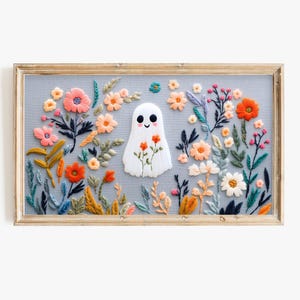 Könnte beinhalten: Stickerei mit einem weißen Geist mit lächelndem Gesicht, umgeben von bunten Blumen in einem Holzrahmen.