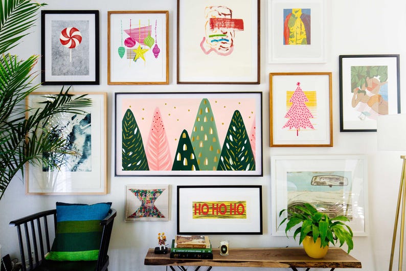 Puede incluir: Una pared de galer&iacute;a con una variedad de obras de arte enmarcadas, que incluyen pinturas abstractas, ilustraciones y una impresi&oacute;n de un bast&oacute;n de caramelo. La pared est&aacute; pintada de blanco y presenta una silla negra con un coj&iacute;n a rayas azul y verde. Las obras de art incluyen una impresi&oacute;n de un &aacute;rbol de Navidad, una impresi&oacute;n de un bosque y una impresi&oacute;n con el texto "Ho Ho Ho".