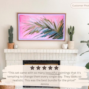 Op de afbeelding: Een digitaal kunstdisplay met een roze en groen palmbladontwerp in een houten frame. Het kunstwerk wordt weergegeven boven een witte bakstenen open haard, met cactussen en decoratieve items op de schoorsteenmantel. Klantfoto.