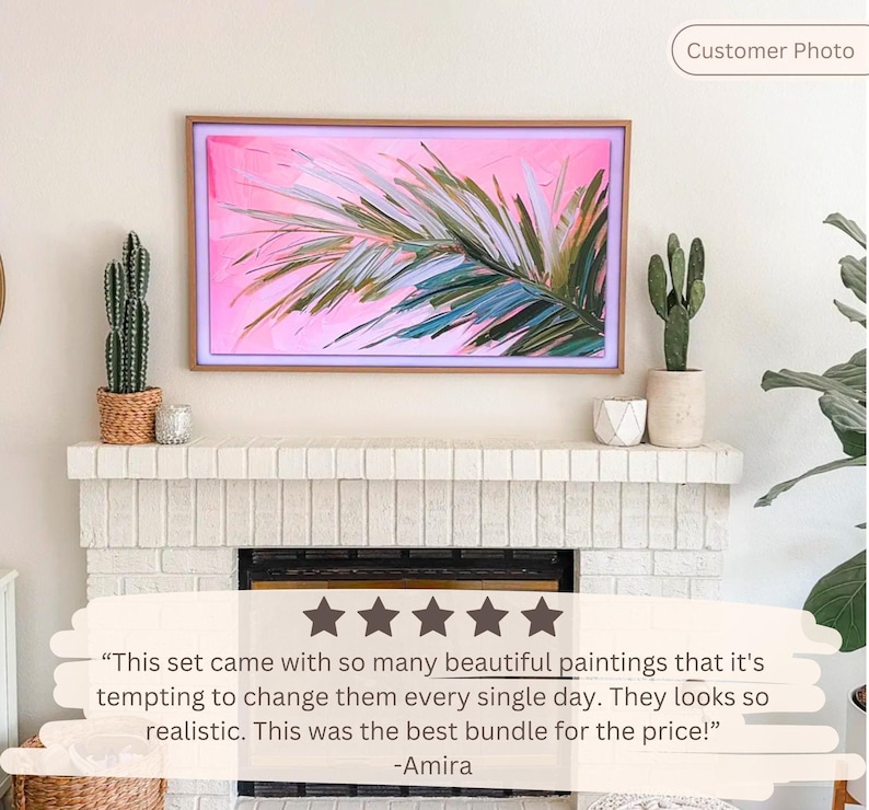 Op de afbeelding: Een digitaal kunstdisplay met een roze en groen palmbladontwerp in een houten frame. Het kunstwerk wordt weergegeven boven een witte bakstenen open haard, met cactussen en decoratieve items op de schoorsteenmantel. Klantfoto.
