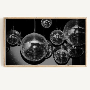 May include: A black and white photograph of multiple disco balls hanging from the ceiling. The disco balls are reflecting light and creating a sparkling effect.
