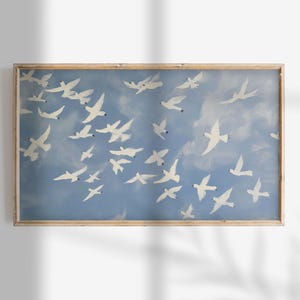 Peut inclure: Une œuvre d'art encadrée représentant un vol d'oiseaux blancs sur un ciel bleu clair avec des nuages doux. Les oiseaux sont représentés dans diverses positions, créant un effet de mouvement. L'œuvre est dans un cadre en bois brun clair.