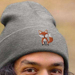 Puede incluir: Un gorro gris con un pequeño diseño de zorro bordado. El zorro es naranja con el vientre blanco y la nariz negra.