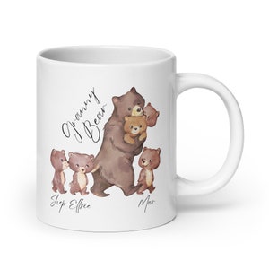 May include: White ceramic mug with a brown bear illustration. The bear is holding two smaller bears. The text "Granny Bear" is written in cursive above the bear. The text "Shep Elfie Max" is written below the bear.