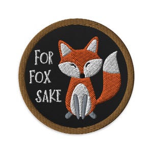 Peut inclure: Un patch rond brodé de couleur marron avec un fond noir. Le patch représente un renard de dessin animé avec un ventre blanc et une pointe blanche sur sa queue. Le texte "FOR FOX SAKE" est brodé en blanc sur le patch.