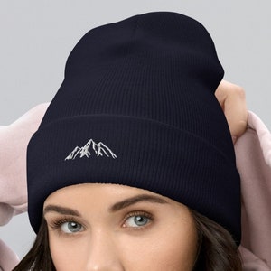 May include: A navy blue beanie with a white embroidered mountain range design.