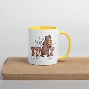 May include: White ceramic mug with a yellow rim. The mug features a watercolor illustration of a brown bear with three cubs. The text "Mama Bear" is written in cursive above the bears. The cubs are labeled "James", "Joan", and "Jessica".