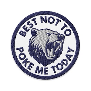 Peut inclure: Un écusson rond blanc brodé avec une bordure bleue. L'écusson représente un ours grognant avec des dents blanches et un visage bleu et gris. Le texte sur l'écusson est "Best not to poke me today".