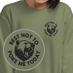 Può includere: Felpa verde con un'immagine di un orso nero e il testo "Best not to poke me today" in un cerchio.
