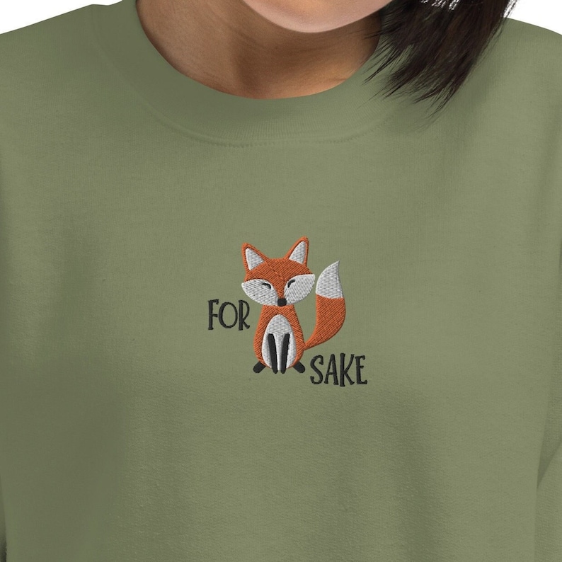 Pu&ograve; includere: Una felpa verde con una volpe ricamata e il testo "FOR FOX SAKE".