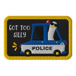 May include: A black and yellow embroidered patch with a cartoon penguin wearing sunglasses driving a blue and white police car. The text "GOT TOO SILLY" is above the car and "POLICE" is written on the side of the car.