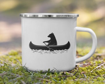 May include: White enamel camping mug with a black silhouette of a bear paddling a canoe on a lake.