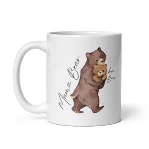 May include: White ceramic mug with a brown bear illustration holding a smaller brown bear. The text "Mama Bear" is written on the left side of the mug and "Luca Bear" is written on the right side.