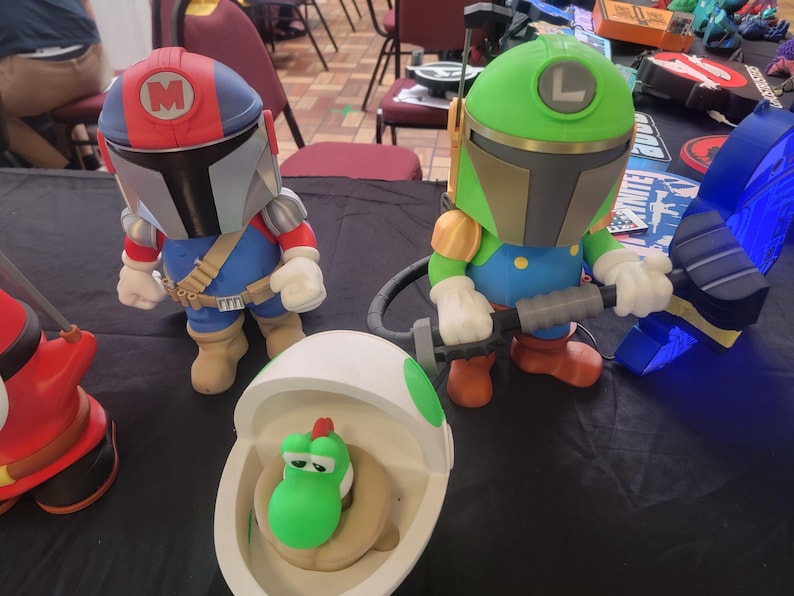Pode incluir: Tr&ecirc;s figuras de brinquedo, uma figura de estilo mandaloriano vermelha e azul com um 'M' no capacete, uma figura verde e azul com um 'L' no capacete, e uma figura verde Yoshi dentro de um ovo branco.