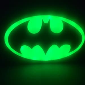 May include: A green glowing Batman logo, a popular superhero symbol, is illuminated against a black background.