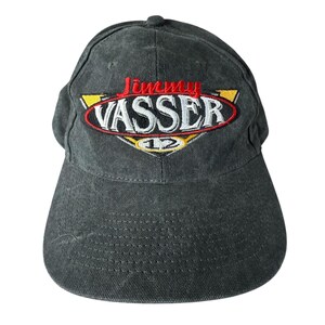 May include: A charcoal gray baseball cap with the embroidered text "Jimmy Vasser" in red and white, with yellow accents. The cap features a curved brim and a rounded top.