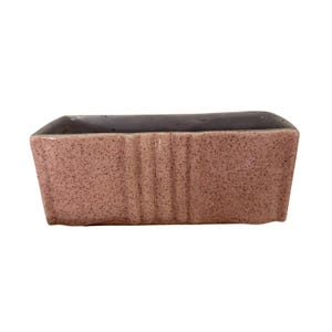 May include: A rectangular ceramic planter featuring a speckled dusty pink exterior finish. The front side displays three vertical recessed grooves centered on the surface. The interior of the vessel is a smooth, light gray color with a wide opening.
