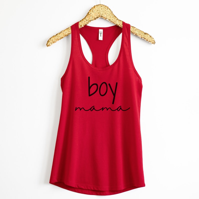Puede incluir: Una camiseta sin mangas roja con las palabras "boy mama" impresas en escritura negra. La camiseta sin mangas est&aacute; colgada de una percha dorada con lentejuelas sobre un fondo blanco. La parte superior est&aacute; hecha de un material suave.