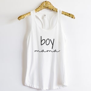 Puede incluir: Camiseta sin mangas blanca con las palabras "boy mama" impresas en escritura negra. La camiseta sin mangas est&aacute; colgada de una percha dorada con lentejuelas. Una camiseta informal y c&oacute;moda para el uso diario.