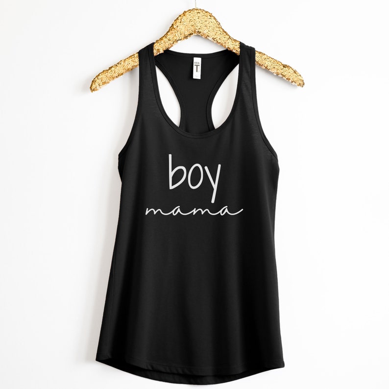 Puede incluir: Camiseta sin mangas negra con las palabras "boy mama" en escritura blanca. La camiseta est&aacute; colgada de una percha dorada sobre un fondo blanco. El texto est&aacute; centrado en la parte delantera.