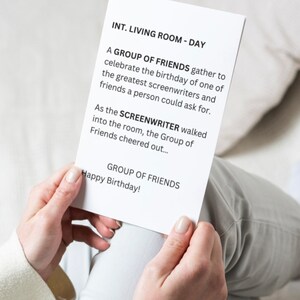 Puede incluir: Una tarjeta blanca con texto negro es sostenida por una persona. La tarjeta dice "INT. LIVING ROOM - DAY" y describe una celebración de cumpleaños para un guionista. La tarjeta también dice "¡Feliz Cumpleaños!"