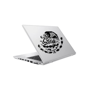 May include: A silver laptop with a black vinyl decal on the lid featuring the Mexican coat of arms, which depicts an eagle perched on a cactus while holding a snake in its beak, surrounded by a wreath of oak and laurel branches.